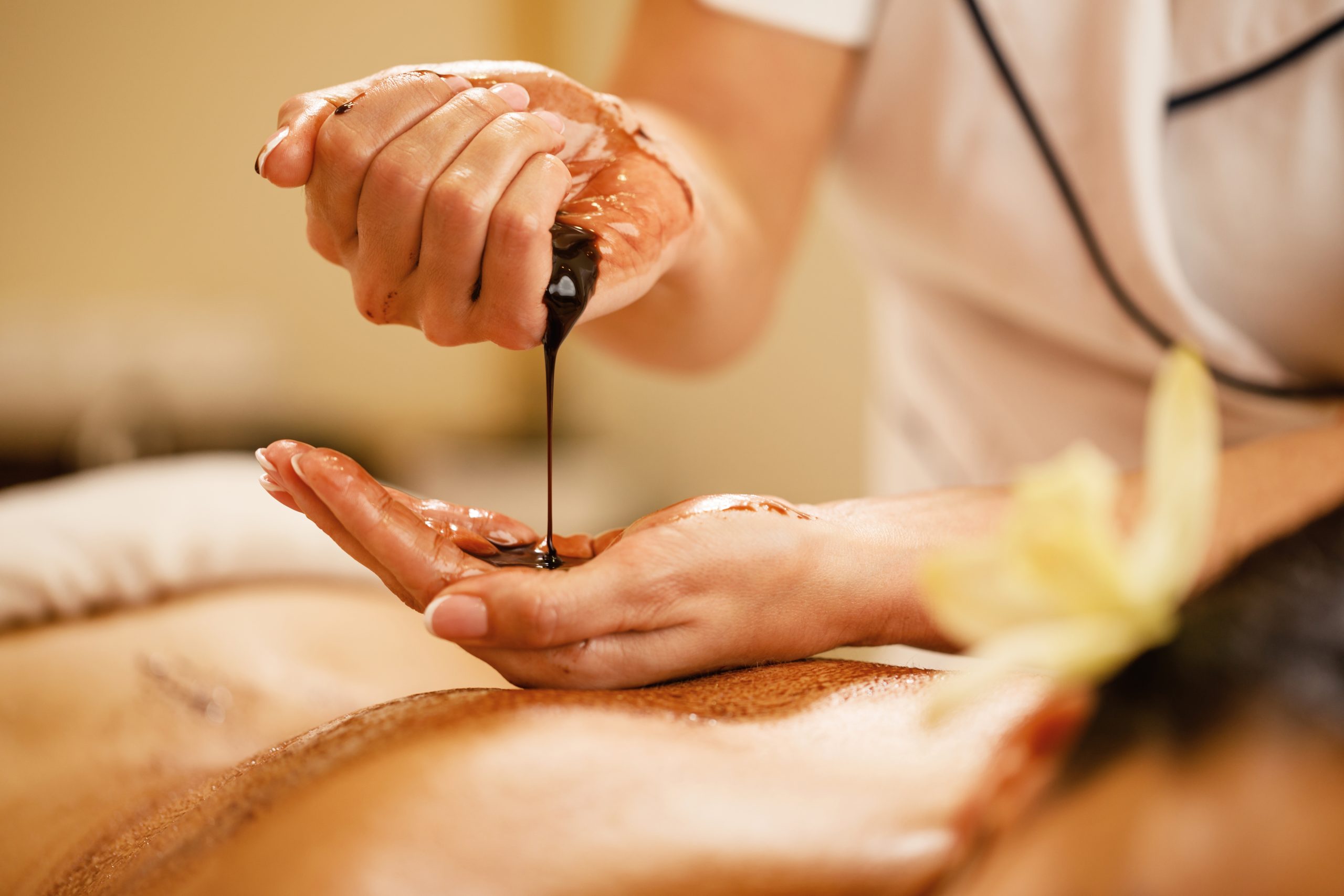 Close-up of massage therapist pouring hot chocolate in her hands before spa treatment.